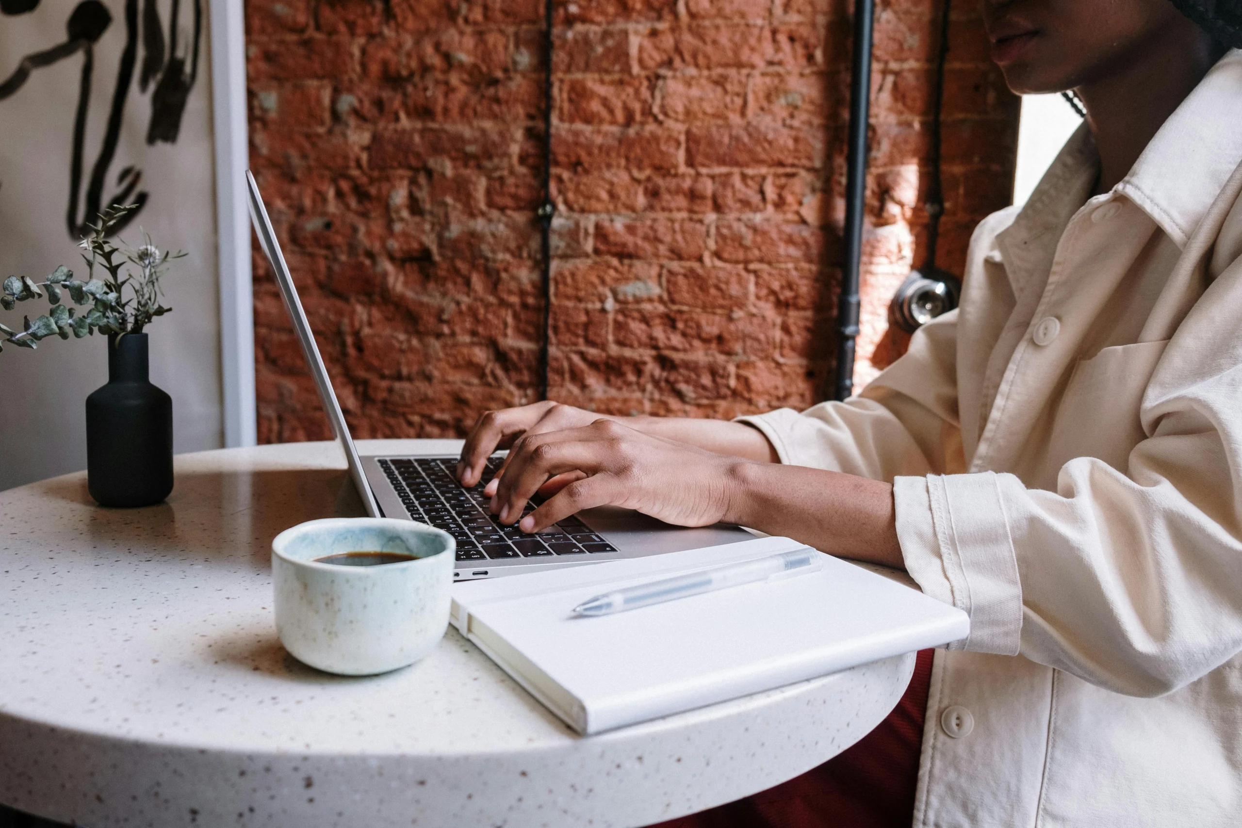 A woman sits at a small circular table writing a blog post on her computer