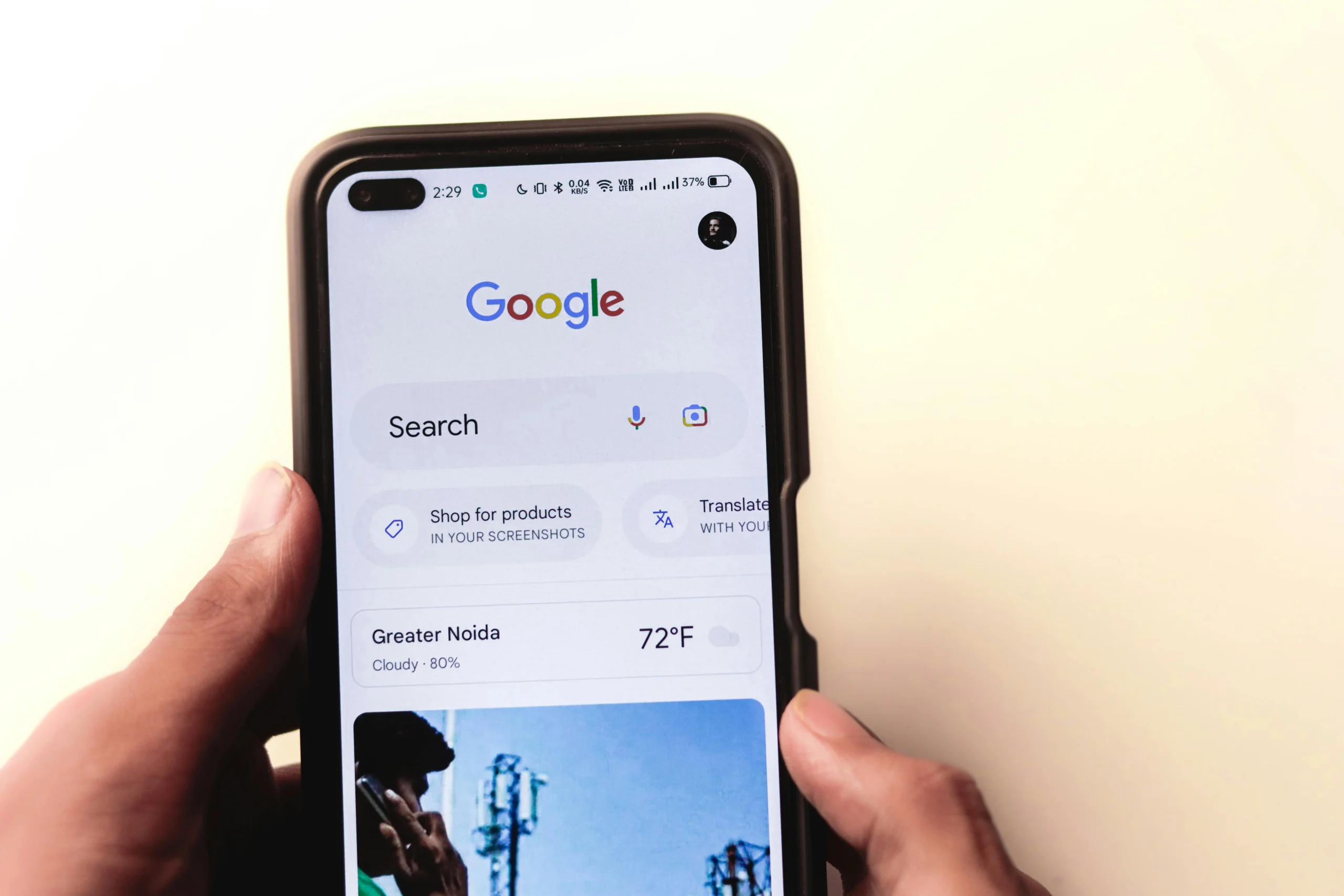 Person holding a smartphone displaying the Google search app on the home screen with the Google logo and search bar visible.